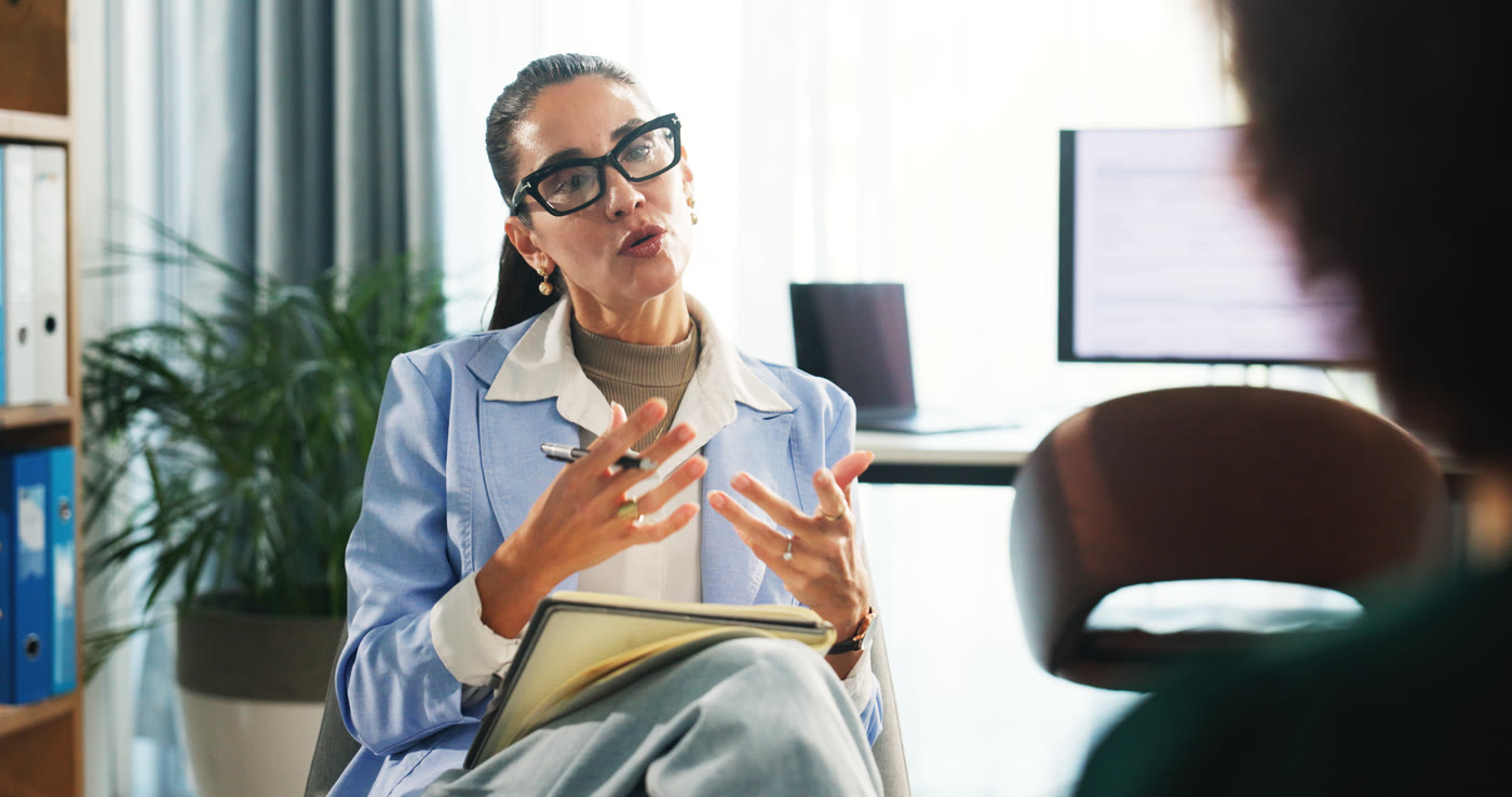 Seated woman with a notebook speaking with a person sitting opposite her